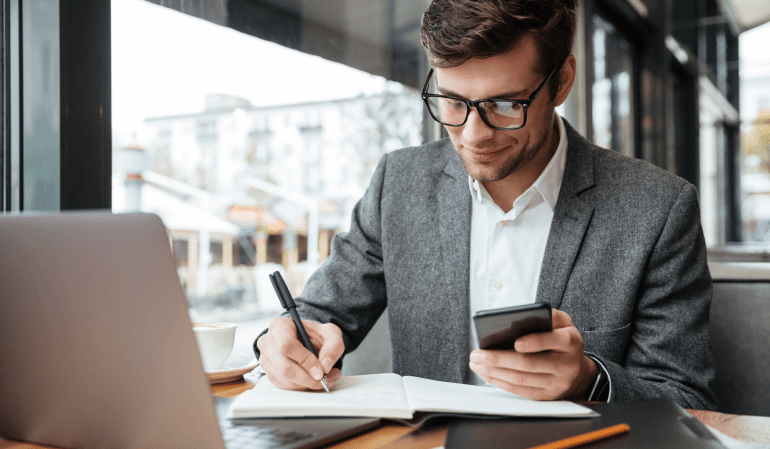 Homem usando o celular e anotando no caderno